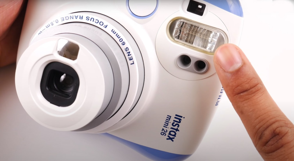 a finger pointing at the flash of the Instax 26 cam showcasing the smart flash functionality