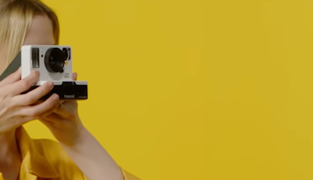 Woman in yellow using a Polaroid camera.